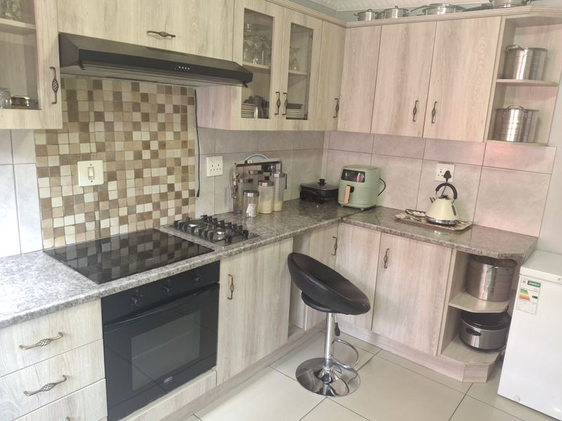 A functional kitchen featuring light wood-grain cabinetry, granite-look laminate countertops, a mosaic tile backsplash, and integrated cooking appliances.