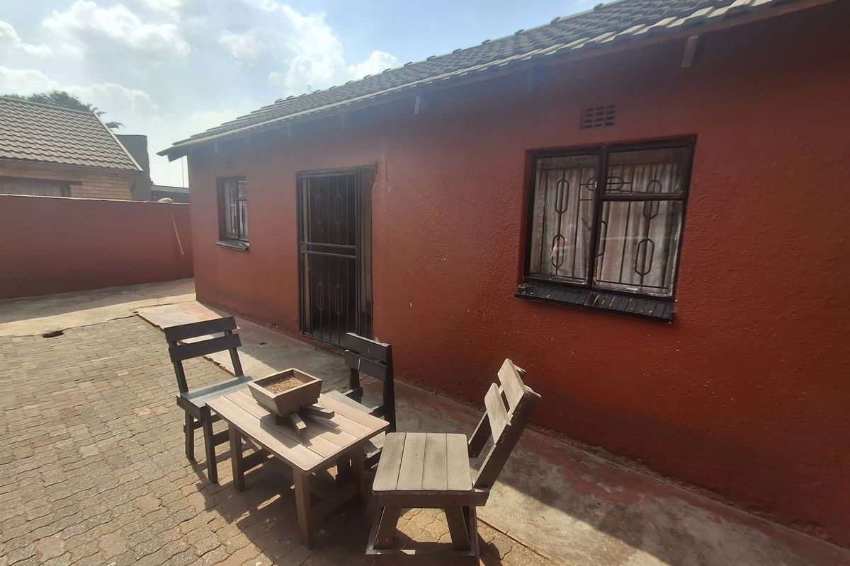 Rear exterior view of the property featuring a paved patio area, security gates, and burglar bars on the windows.