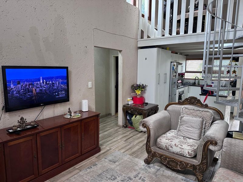 Open plan living area featuring a spiral staircase leading to a mezzanine level, tiled flooring, and an integrated kitchen space with built-in cabinetry.