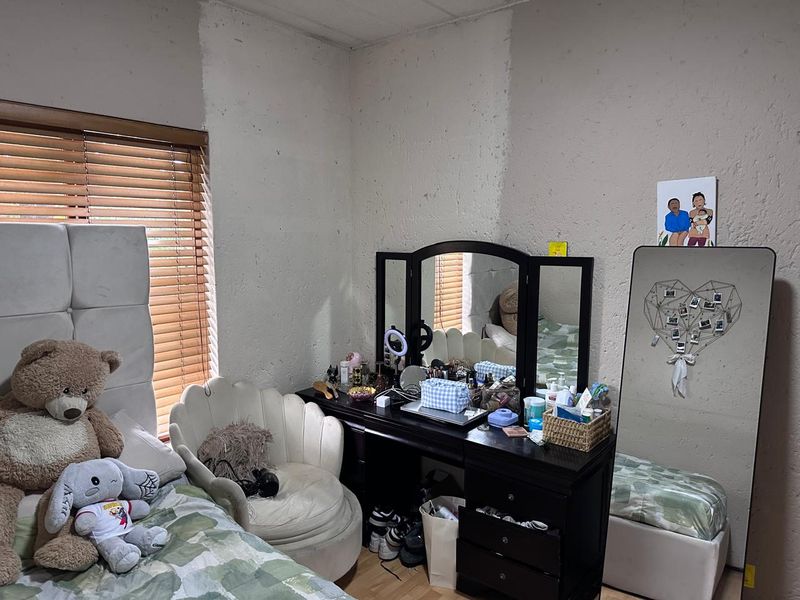 A bedroom featuring laminate flooring and venetian blinds, currently showing signs of wear on the wall surfaces.