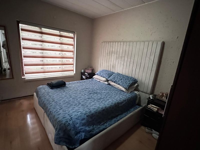 A bedroom featuring laminate flooring and window blinds, currently showing signs of wall surface deterioration requiring maintenance or cosmetic repair.