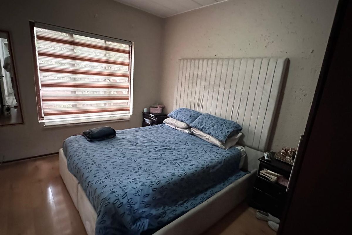 A bedroom featuring laminate flooring and window blinds, currently showing signs of wall surface deterioration requiring maintenance or cosmetic repair.
