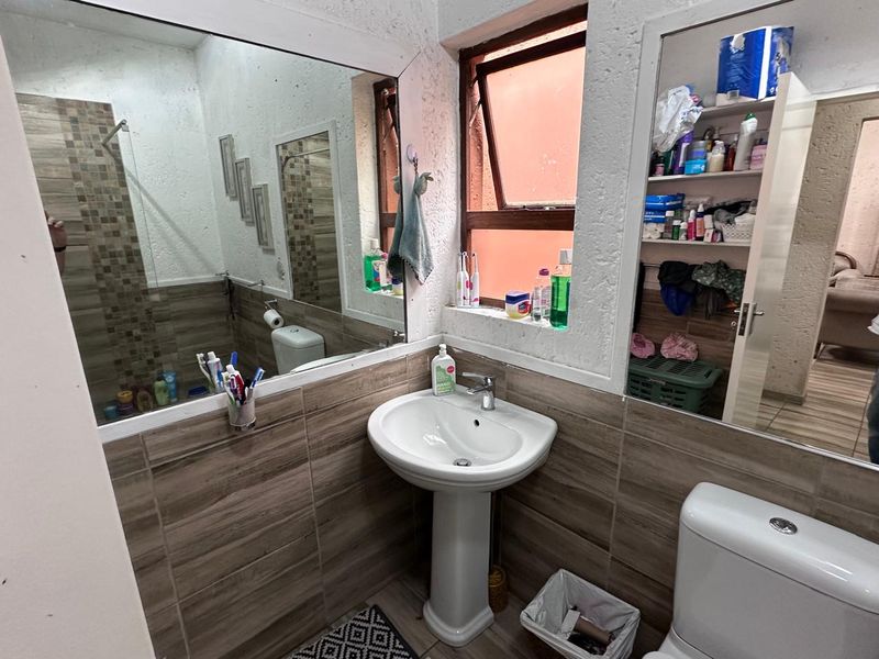 A functional bathroom featuring a pedestal basin, toilet, and tiled finishes with a large wall mirror and natural light from a top-hung window.