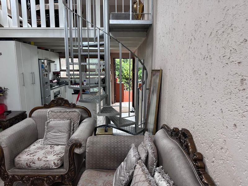 Open plan living area featuring a metal spiral staircase leading to a mezzanine level, adjacent to a functional kitchen space.