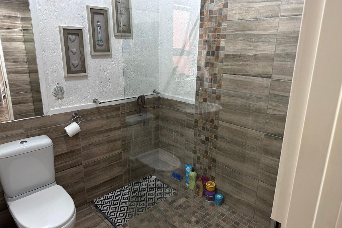 A modern bathroom featuring a walk-in shower with glass screen, wood-look wall tiles, and decorative mosaic accents.