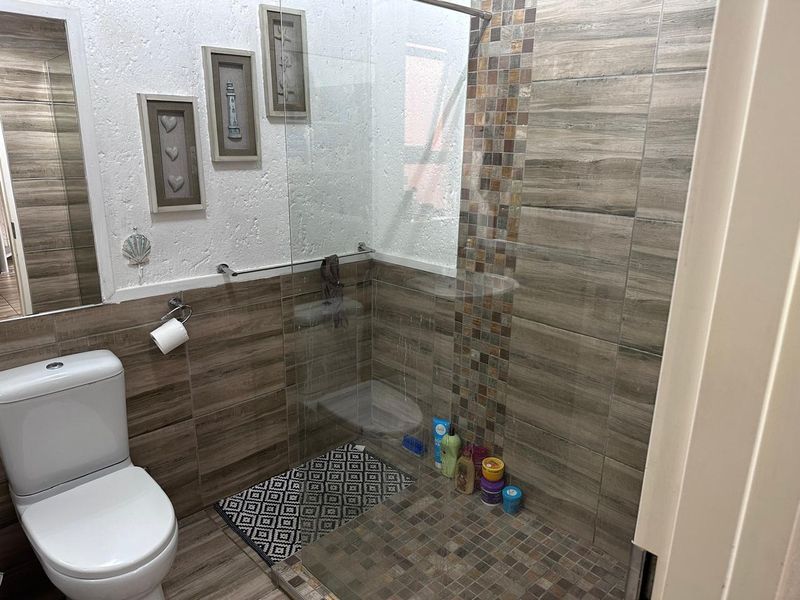 A modern bathroom featuring a walk-in shower with glass screen, wood-look wall tiles, and decorative mosaic accents.