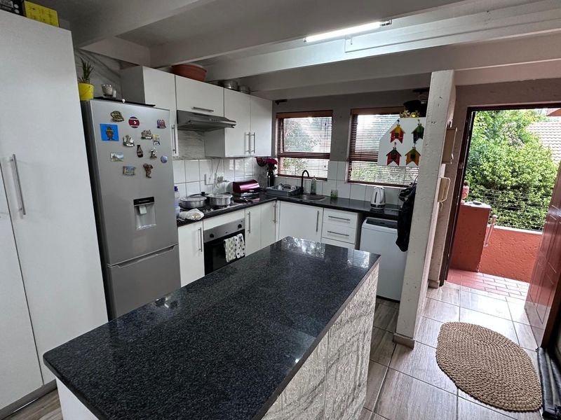 Functional kitchen featuring granite countertops, built-in cabinetry, oven, extractor fan, and direct access to an outdoor patio area.