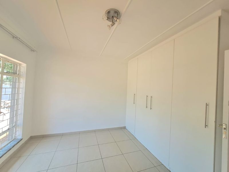 A clean, empty bedroom featuring neutral tiled flooring, white walls, and extensive built-in cupboard storage with modern hardware.