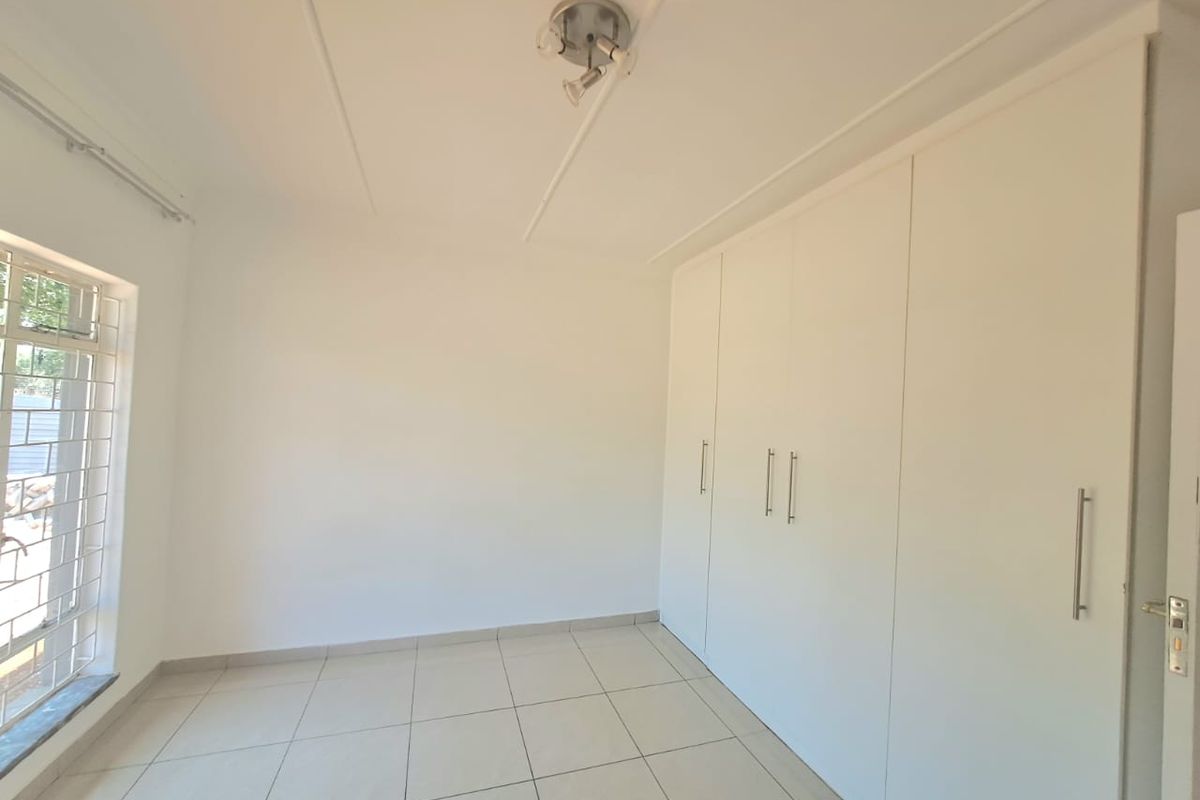 A clean, empty bedroom featuring neutral tiled flooring, white walls, and extensive built-in cupboard storage with modern hardware.