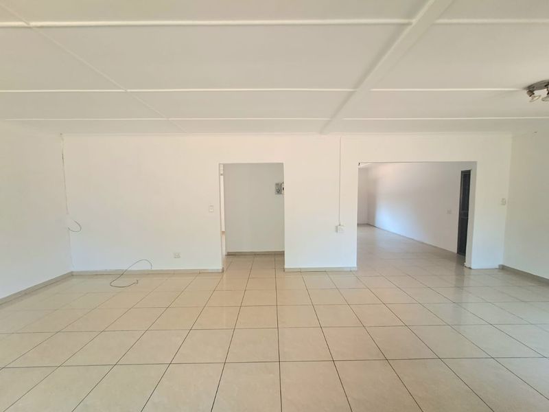 A spacious, empty open-plan living area featuring neutral tiled flooring and a simple ceiling design, offering a blank canvas for interior customization.