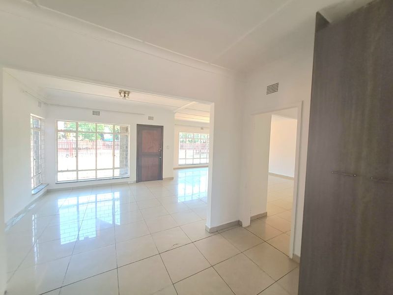 Spacious open-plan living area featuring neutral tiled flooring, large windows for natural light, and a built-in cupboard, offering a bright and versatile layout.