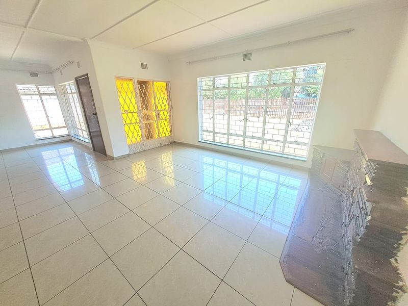Spacious, light-filled living area featuring large windows, neutral tiled flooring, and a characterful built-in stone fireplace.