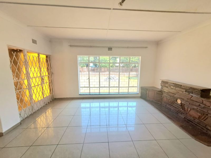 Spacious, empty living room featuring large windows, tiled flooring, and a prominent stone-clad fireplace feature, offering a bright and versatile living space.