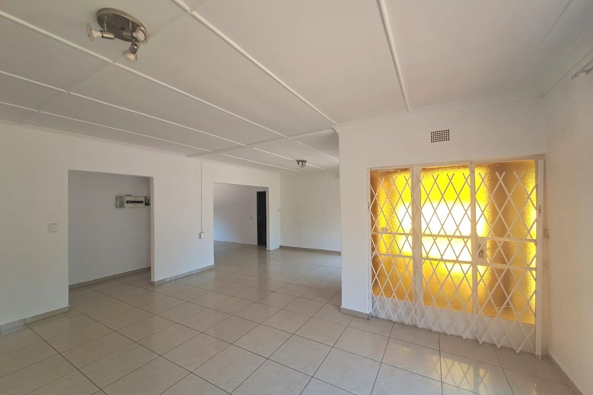 Spacious, empty living area featuring neutral tiled flooring, white ceiling panels, and a secure metal gate entrance.