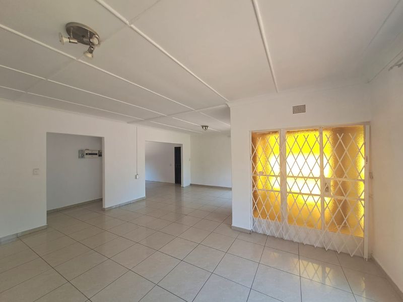 Spacious, empty living area featuring neutral tiled flooring, white ceiling panels, and a secure metal gate entrance.