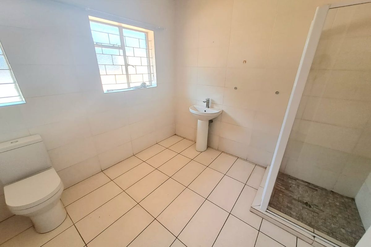 A functional, empty bathroom featuring a pedestal basin, toilet, and a glass-enclosed shower with neutral floor and wall tiling.