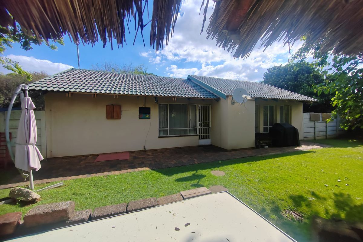 Rear view of the house featuring a paved patio area, lawn, and tiled roof structure with a satellite dish installed.
