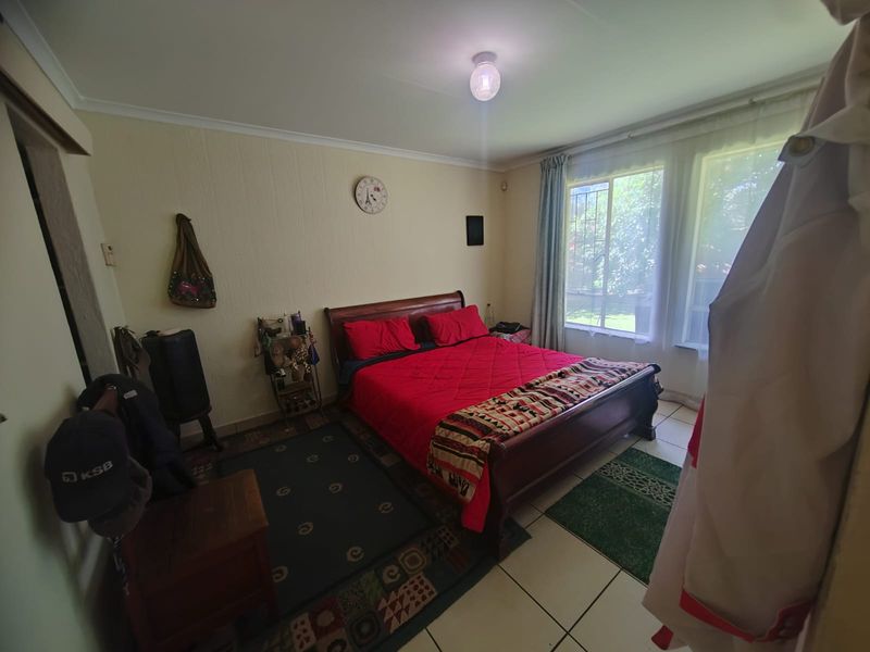 A functional bedroom featuring tiled flooring, a built-in cupboard, and a window fitted with security bars, offering natural light and a practical layout.