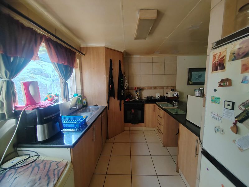A functional kitchen featuring built-in cabinetry, a double sink, tiled backsplash, and integrated oven and hob, with tiled flooring throughout.
