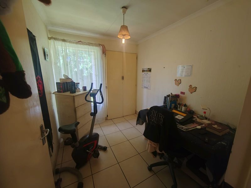 A compact bedroom featuring tiled flooring, a built-in wardrobe, and a window with security bars, offering a functional space for a bedroom or home office.