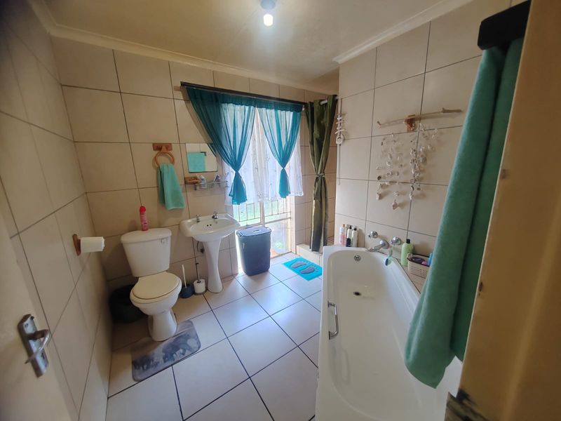 A functional bathroom featuring a pedestal basin, toilet, and bathtub with full-height wall tiling and tiled flooring.