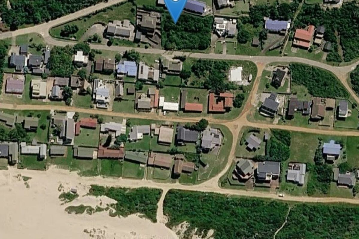 An aerial view of a residential vacant land plot situated in a coastal neighborhood, showing surrounding properties and proximity to the beach.