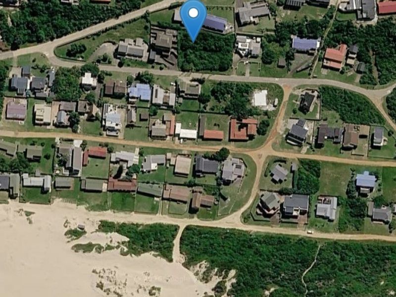 An aerial view of a residential vacant land plot situated in a coastal neighborhood, showing surrounding properties and proximity to the beach.
