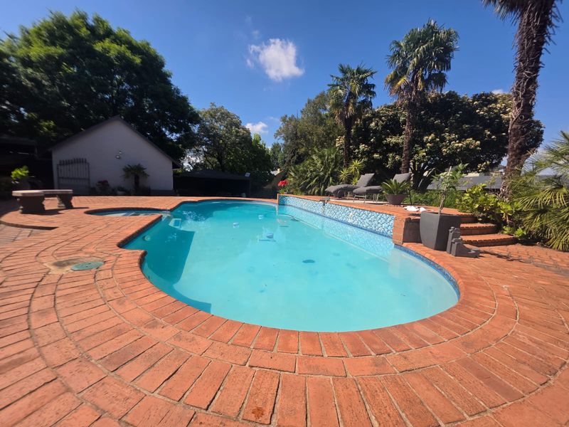 Outdoor swimming pool area featuring a curved design, tiled water feature, and surrounding brick paved patio set within a landscaped garden.