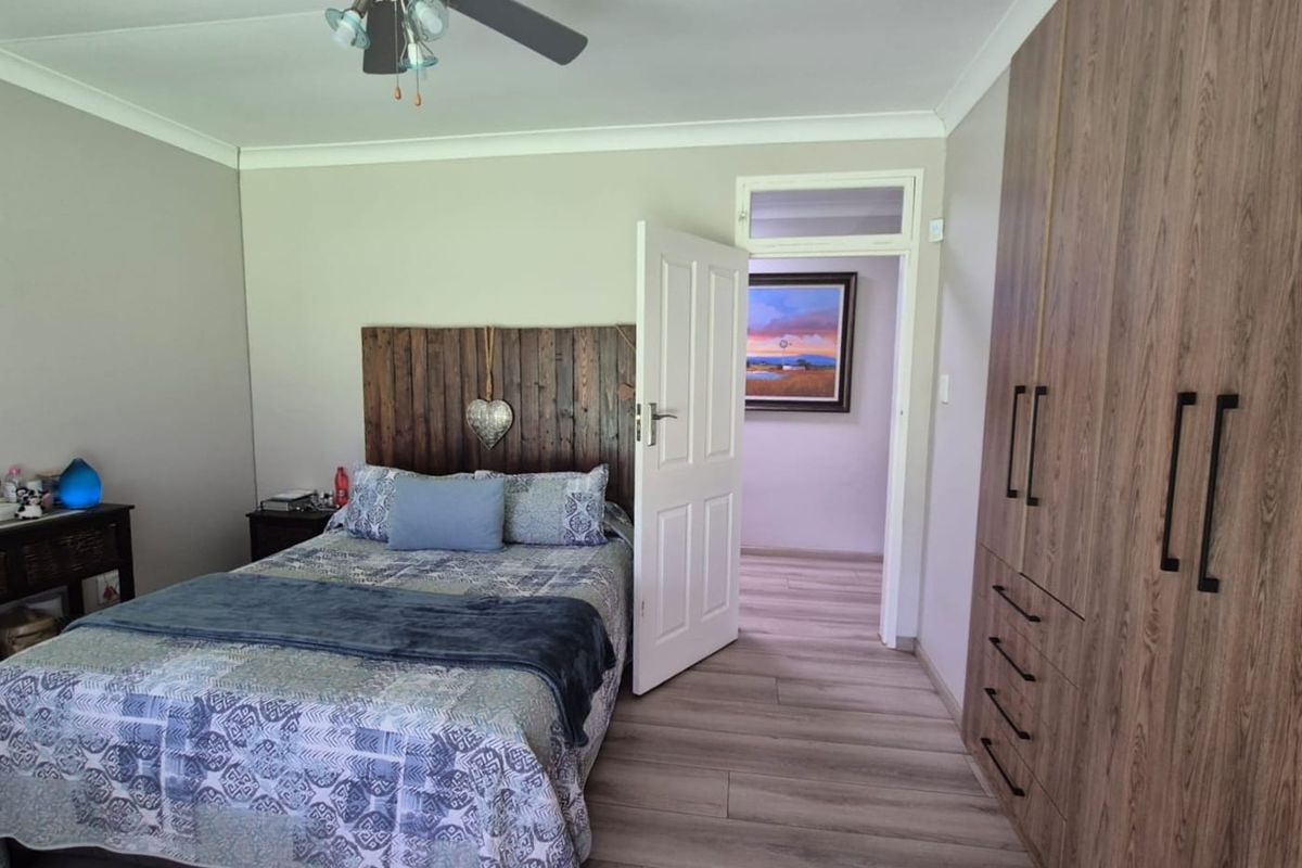 A well-maintained bedroom featuring modern laminate flooring, built-in wooden cupboards, and a ceiling fan, offering a clean and functional living space.