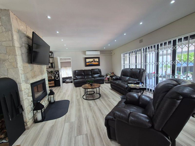 Spacious living room featuring a prominent stone-clad fireplace, modern wood-look flooring, recessed lighting, and large sliding doors providing access to the outdoor area.