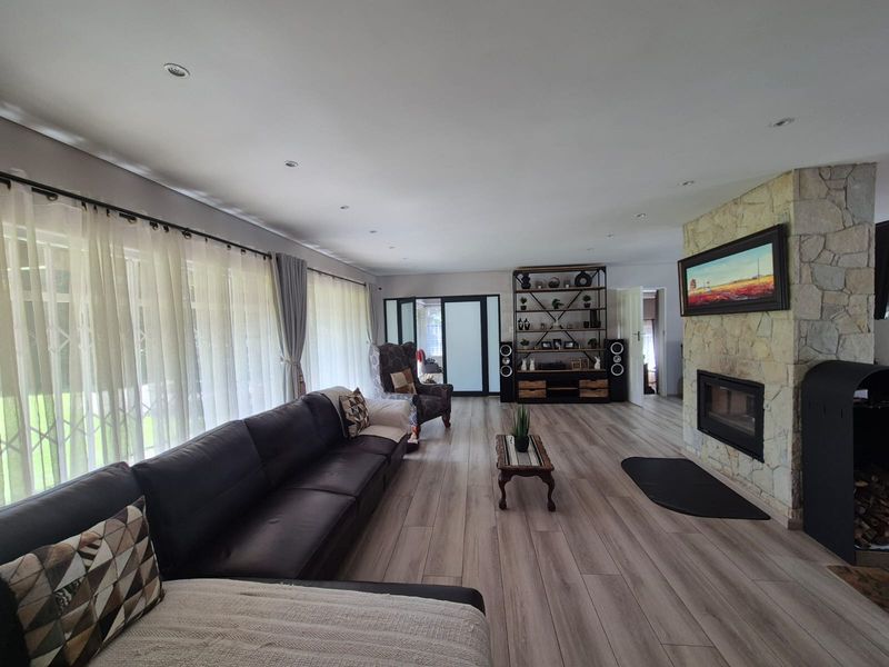 Spacious living room featuring a prominent stone-clad fireplace, modern laminate flooring, and large windows with natural light.