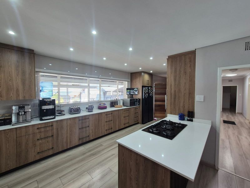 Modern kitchen featuring wood-grain cabinetry, quartz countertops, a central island with a gas hob, and recessed lighting.