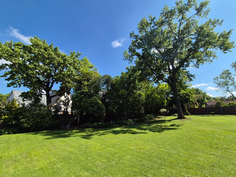 A spacious, well-maintained garden featuring a large, manicured lawn and mature trees, providing a private and serene outdoor setting.