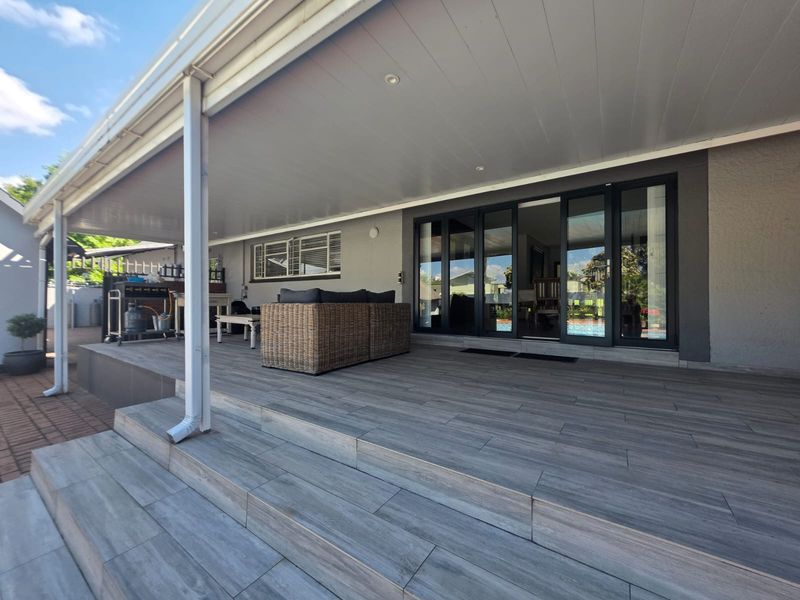 A spacious covered patio featuring modern wood-look tiled flooring, recessed ceiling lights, and large sliding glass doors providing seamless indoor-outdoor flow.