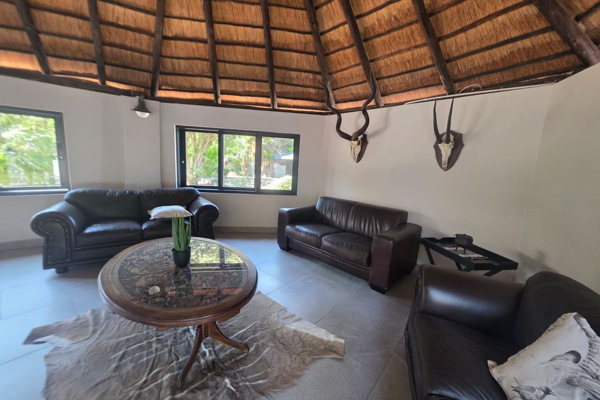 Spacious living area featuring a traditional thatched roof with exposed timber rafters, tiled flooring, and large windows providing natural light.