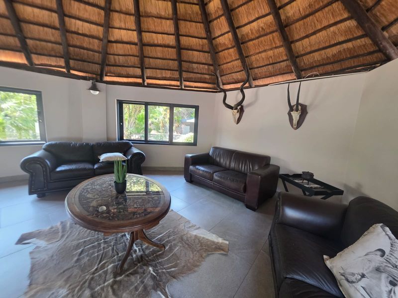 Spacious living area featuring a traditional thatched roof with exposed timber rafters, tiled flooring, and large windows providing natural light.