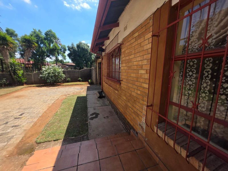 Rear exterior view of the house featuring face brick walls, security bars on windows, a paved driveway, and a tiled patio area.