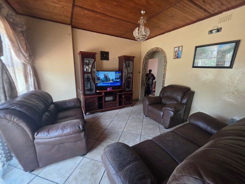 A living room featuring ceramic floor tiles, a timber-paneled ceiling, and a decorative arched doorway with stone-cladding detail.