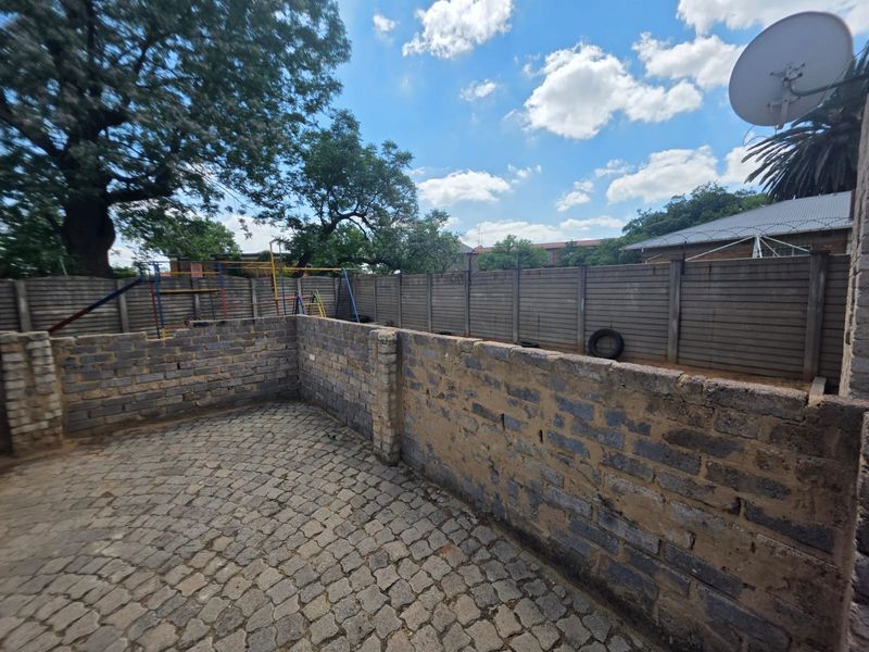 Rear outdoor area featuring cobblestone paving, a low brick retaining wall, and a precast concrete boundary wall.