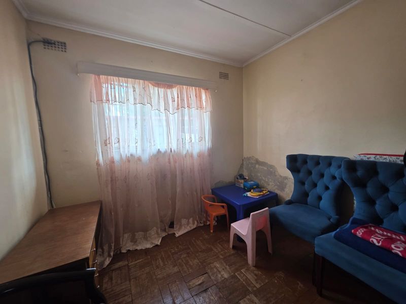 A bedroom featuring parquet flooring and a window, currently showing significant wall plaster damage and peeling paint requiring maintenance.
