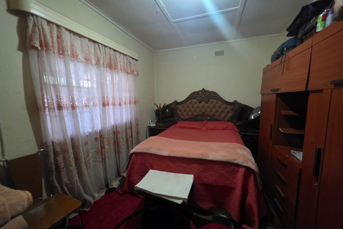 A bedroom featuring a built-in wardrobe and ceiling ventilation, showing signs of wear on the ceiling finishes.