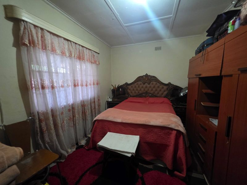 A bedroom featuring a built-in wardrobe and ceiling ventilation, showing signs of wear on the ceiling finishes.