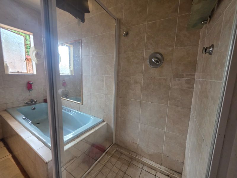 A dated bathroom featuring a built-in bathtub, separate shower enclosure, and neutral wall tiling. The space is ready for a modern renovation.