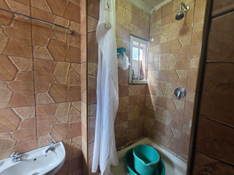 A dated bathroom featuring stone-effect wall tiles, a shower enclosure, and a wall-mounted basin.