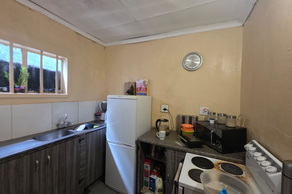 A compact kitchen featuring laminate cabinetry, a stainless steel sink, tiled splashback, and an electric stove with visible wear on the cooktop.