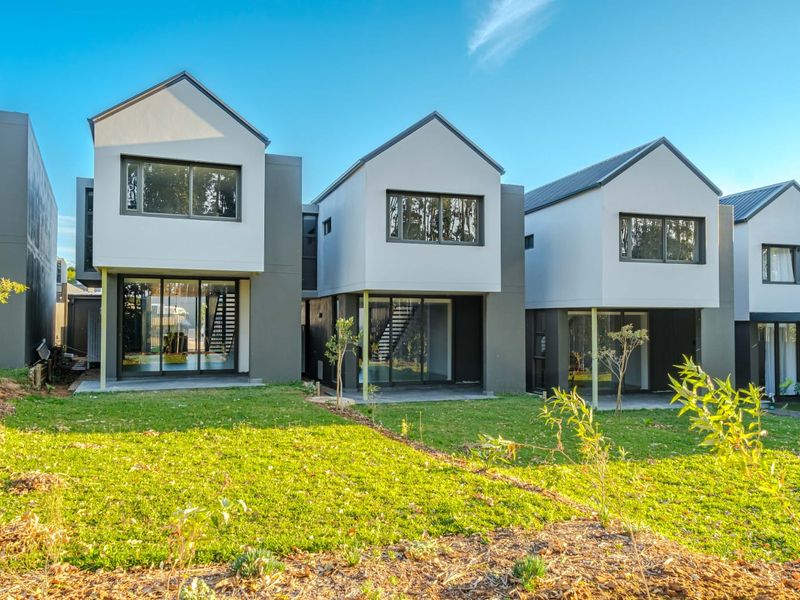 Rear view of modern townhouse complex featuring contemporary architectural design, sliding glass doors, private patio areas, and well-maintained garden spaces.