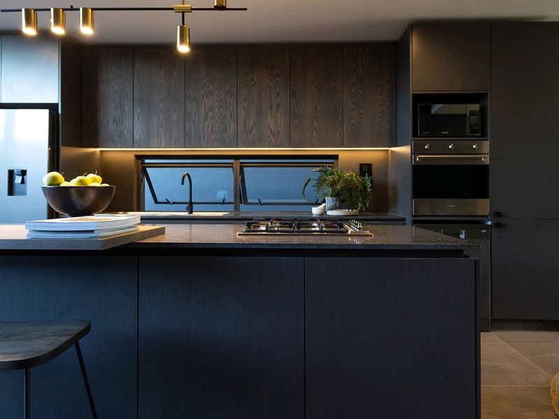 Modern, high-end kitchen featuring dark wood cabinetry, a stone island with integrated gas cooktop, built-in appliances, and sophisticated under-cabinet lighting.