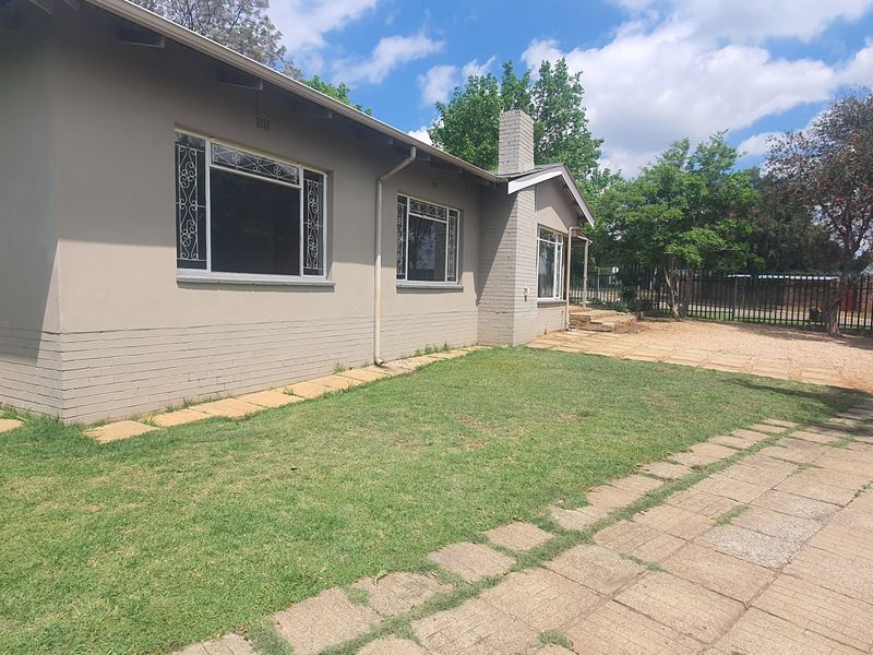 Front exterior view of a single-story house featuring a paved driveway, lawn, and security-barred windows.