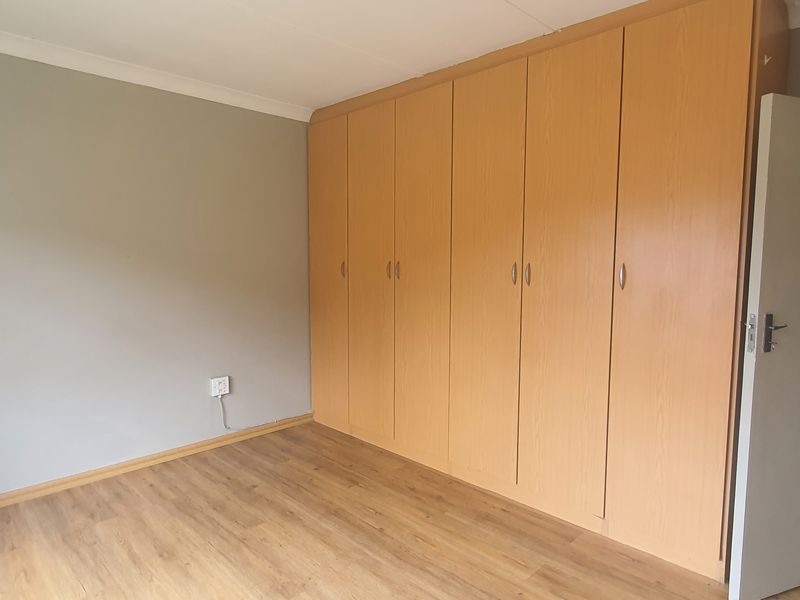 A clean, empty bedroom featuring light wood-look laminate flooring and extensive built-in wooden cupboards.