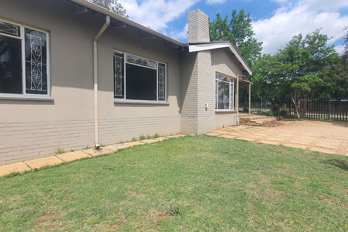 Rear view of the property featuring a brick chimney, paved patio area, and a lawn with perimeter fencing.
